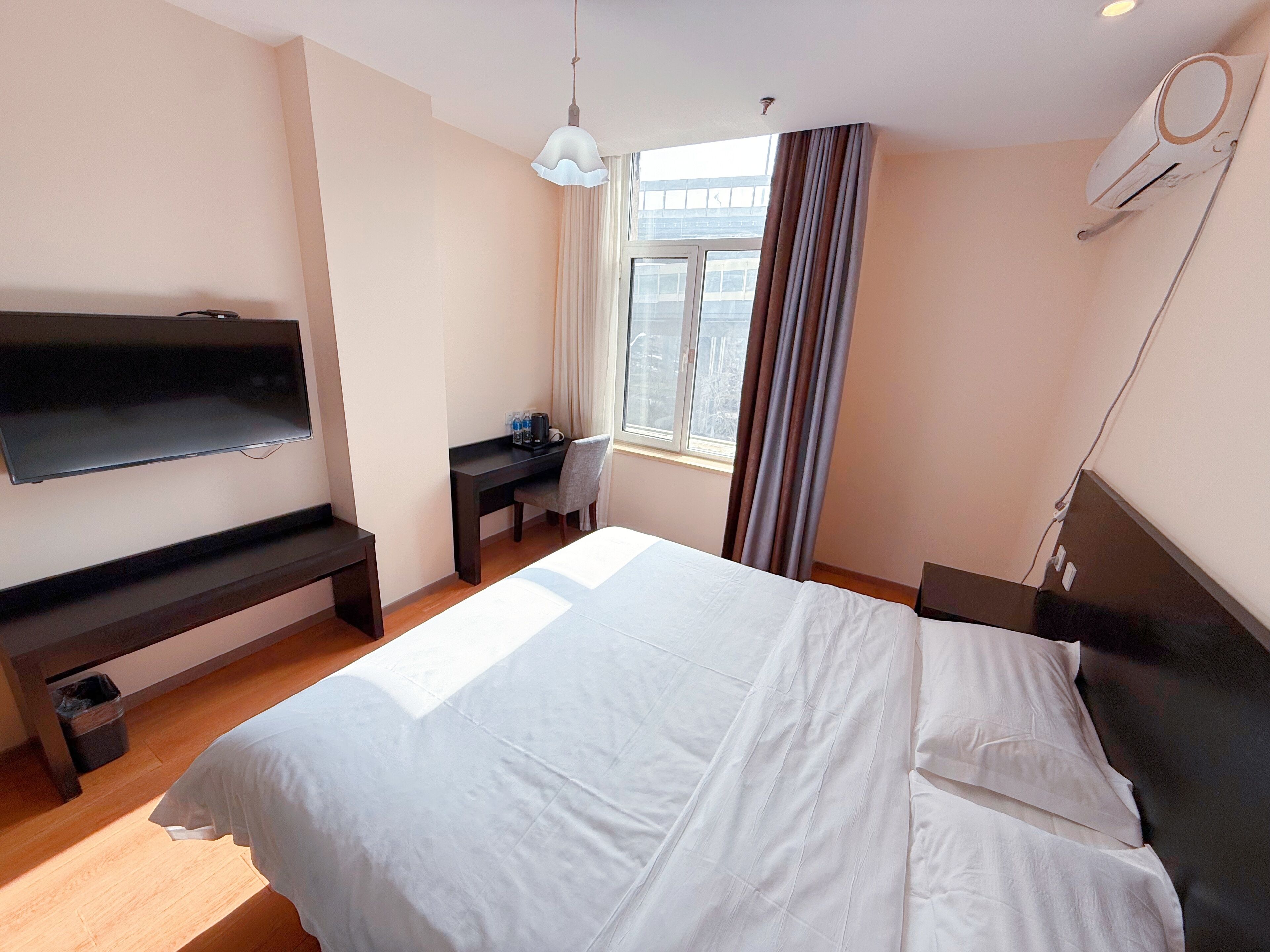 Ein Hotelzimmer mit einem Bett, einem Schreibtisch, einem Stuhl, einem Fernseher und einem Fenster mit Vorhängen.