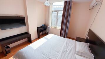 Ein Hotelzimmer mit einem Bett, einem Schreibtisch, einem Stuhl, einem Fernseher und einem Fenster mit Vorhängen.