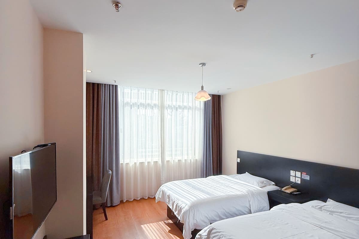 Ein Hotelzimmer mit zwei Betten, einem Fernseher, einem Schreibtisch und einem Fenster mit Vorhängen.