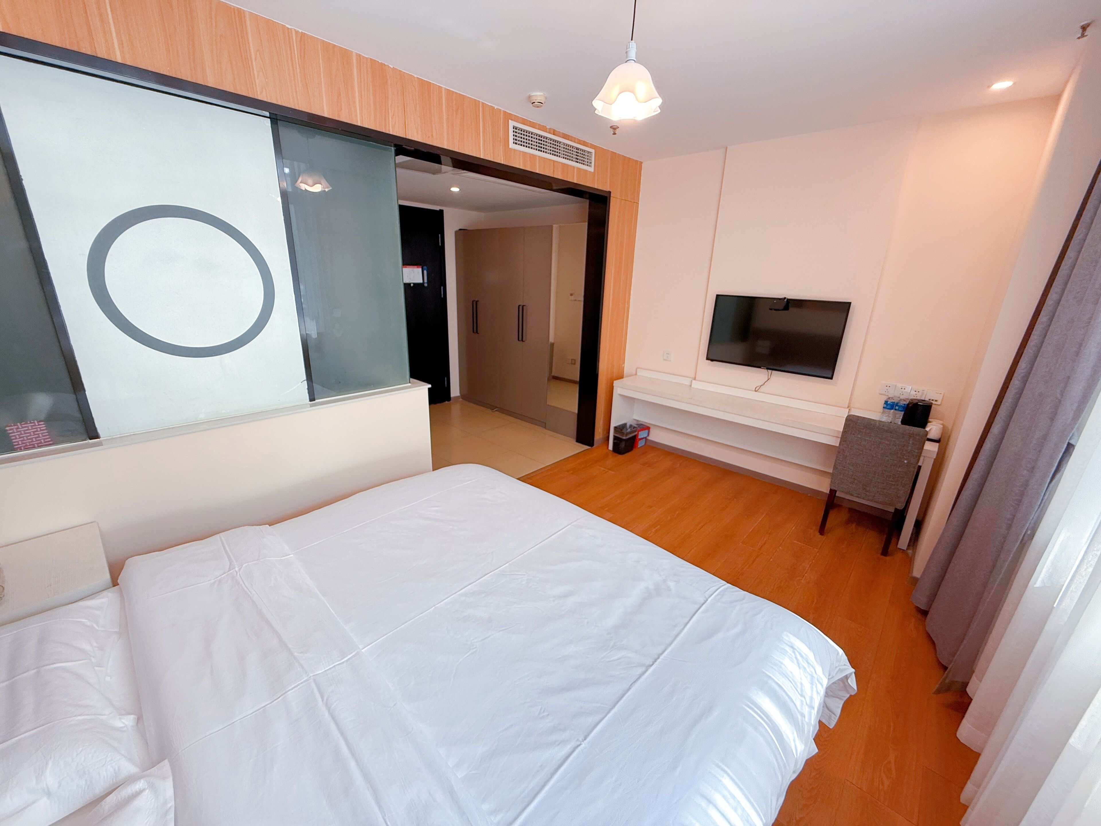 A hotel room with a bed, a TV, a desk, and a large mirror.