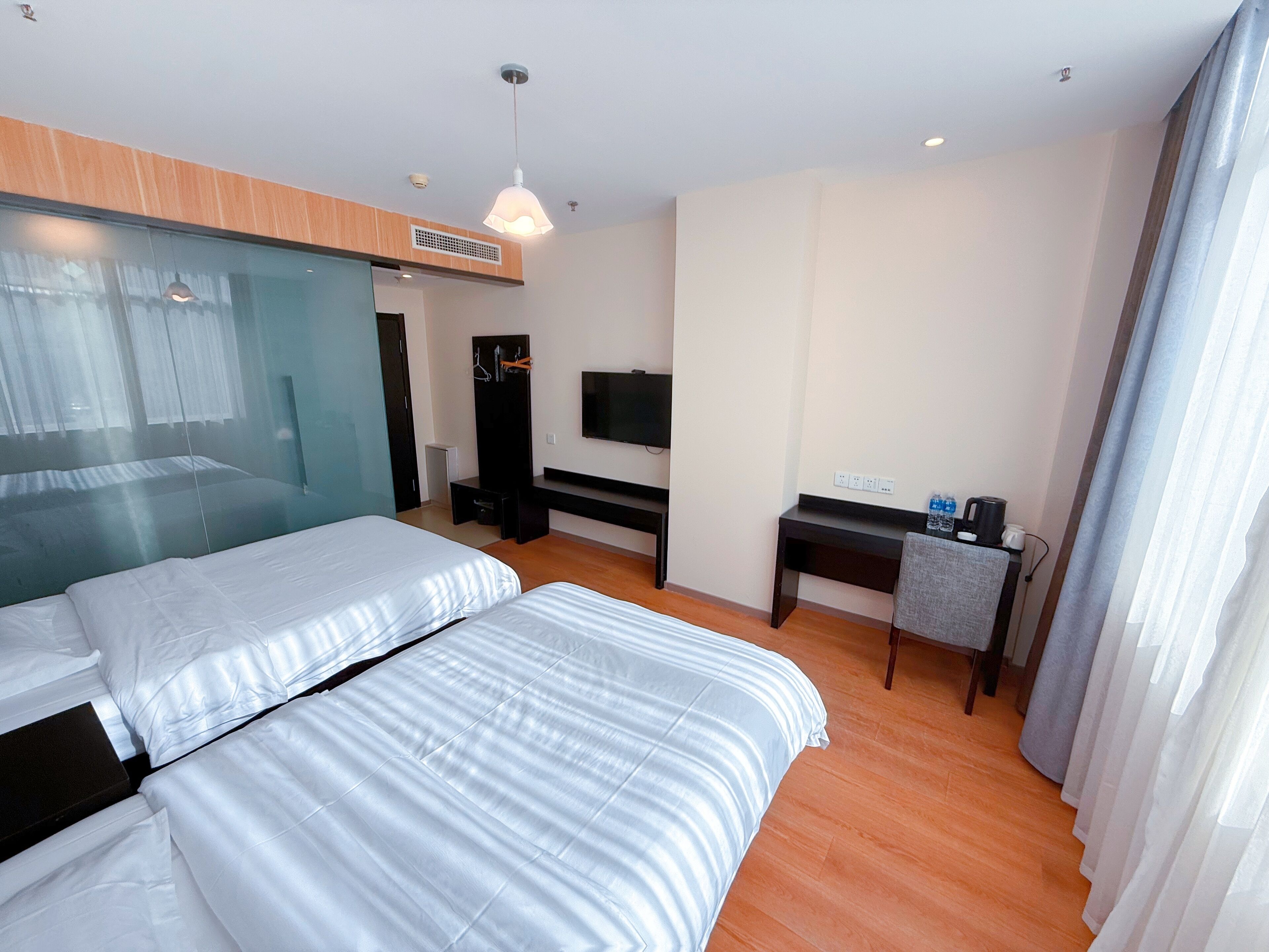 A modern hotel room with two beds, a desk, a television, and a wardrobe.