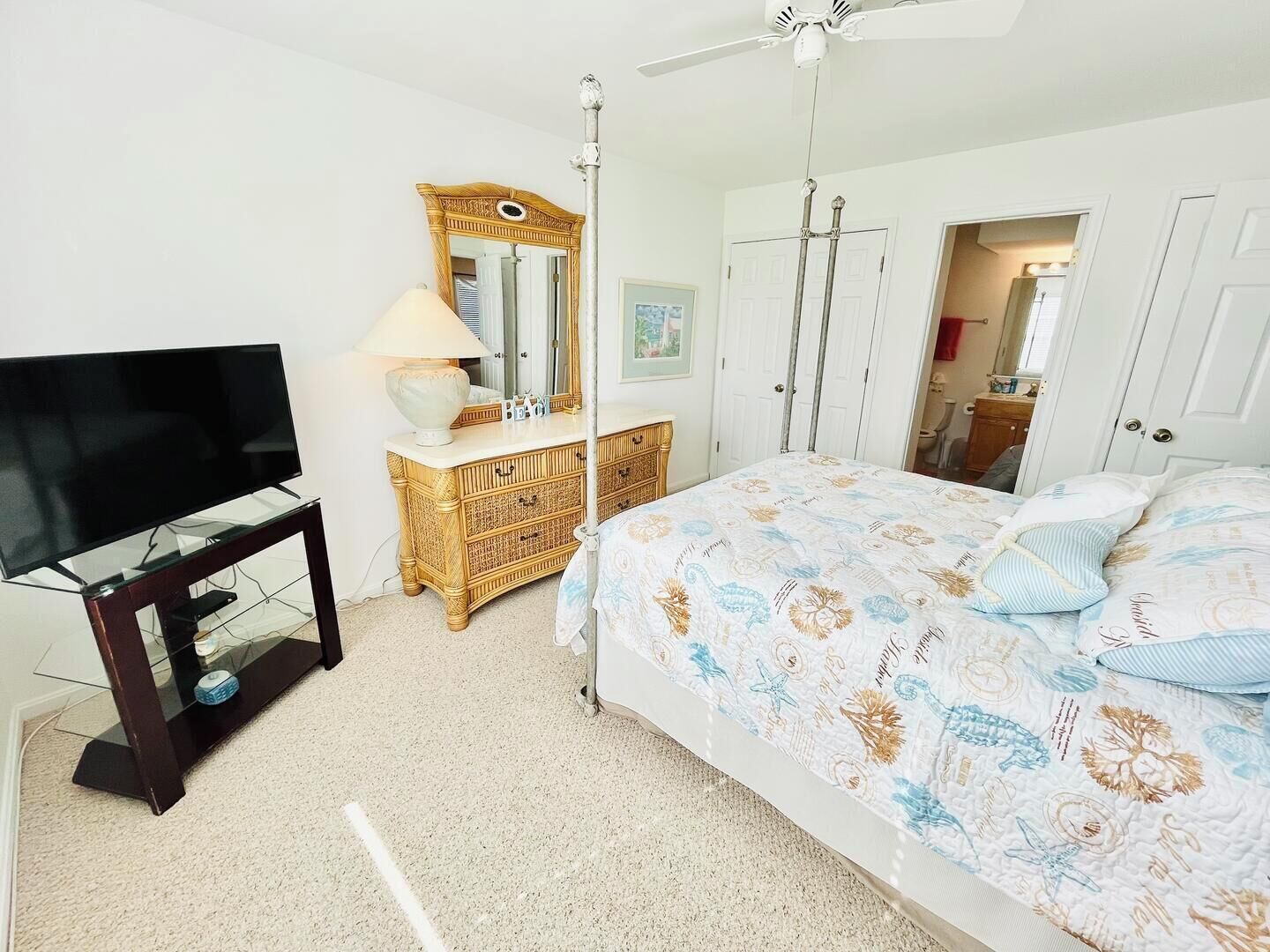 A bedroom with a bed, a television on a stand, a dresser, a mirror, and a ceiling fan.