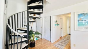 Interior moderno com escada em espiral, planta em vaso e corredor que leva a uma porta com quadro emoldurado.