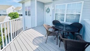 Um deck coberto com mesa e cadeiras, uma porta decorada com uma guirlanda e um corrimão branco.