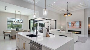 Una cocina moderna con una isla grande, iluminación colgante y un comedor con vistas.