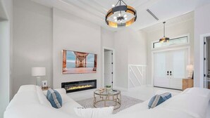 Una sala de estar moderna con un sofá blanco, una chimenea, una mesa de centro redonda y un cuadro grande en la pared.