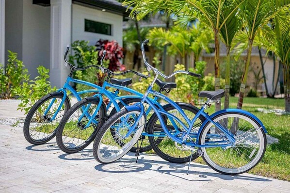 Una fila de bicicletas azules estacionadas en un camino pavimentado en una zona ajardinada con follaje y un edificio al fondo.