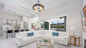 Una sala de estar moderna con un sofá seccional blanco, una mesa de centro de vidrio y un ventanal que ofrece vistas al exterior.