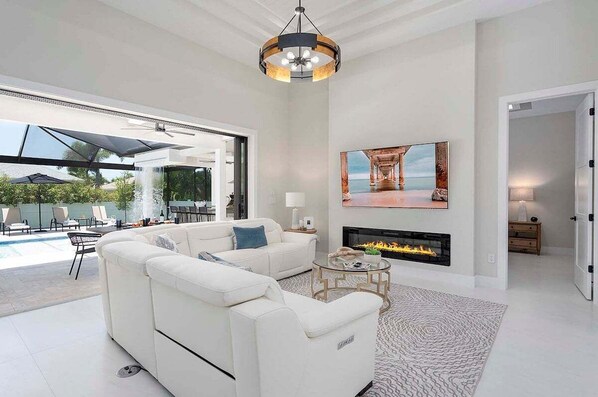 Amplia sala de estar con un sofá blanco, una chimenea, un cuadro grande y vistas a una piscina exterior.