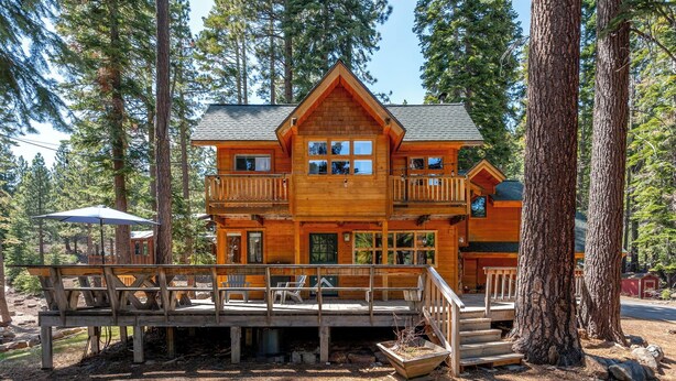 Une cabane en rondins à deux étages, dotée d’un balcon et d’une terrasse, entourée de grands arbres.