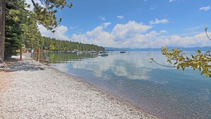 Une vue paisible sur un lac, avec des bateaux, une plage de galets et une zone boisée.