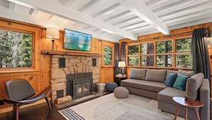 Un salon chaleureux avec une cheminée en pierre, des murs en bois et de grandes fenêtres donnant sur la forêt.