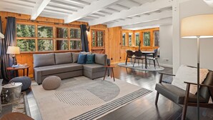 Un salon moderne avec un canapé d’angle, un coin repas et de grandes fenêtres dotées de rideaux.
