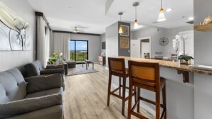 A modern kitchen with a bar area, a dining space with a sofa, and a view of the outdoors. - Origin 1217 - One Bedroom - Partial Gulf View (Panama City Beach)