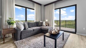 A modern living room with a sectional sofa, a coffee table, and a view of the outdoors through large windows. - Origin 1217 - One Bedroom - Partial Gulf View (Panama City Beach)