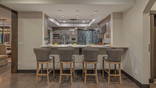 A modern kitchen with a central island, bar stools, and a dining area with a table and chairs. - Spacious + Spectacular + Views | Aspen Glade Retreat (Beaver Creek)
