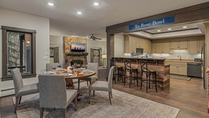 A modern kitchen with a stone fireplace, a dining area with a round table and bar stools, and a sign reading "To Rose Bowl".