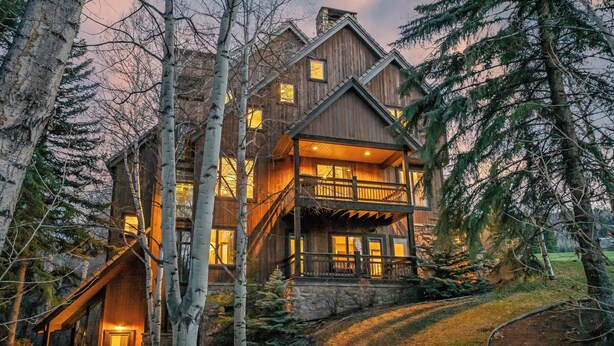Une grande cabane en bois dotée d’un balcon et de nombreuses fenêtres, entourée d’arbres.