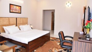 A hotel room with a bed, a desk, a chair, a TV, and a painting on the wall. - Arkaya Inn (Gurugram)