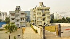 A residential building with multiple floors, a gated entrance, and a parking area. - Arkaya Inn (Gurugram)