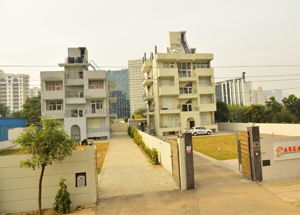 A residential building with multiple floors, a gated entrance, and a parking area. - Arkaya Inn (Gurugram)