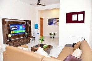 A modern living room with a flat-screen TV, a coffee table, sofas, and a bulletin board. - Arkaya Inn (Gurugram)