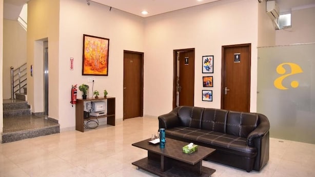 A lobby with a black leather sofa, a coffee table, a fire extinguisher, and framed artwork on the walls. - Arkaya Inn (Gurugram)