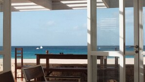A beachside room with a view of the ocean, featuring a wooden table, chairs, and a window overlooking the beach. - 4 Bedroom Private vacation home in Vila do Maio (Vila do Maio)