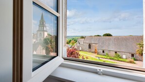 Ein Fenster mit Blick auf ein Kirchturmdach und ein Steingebäude mit Garten.