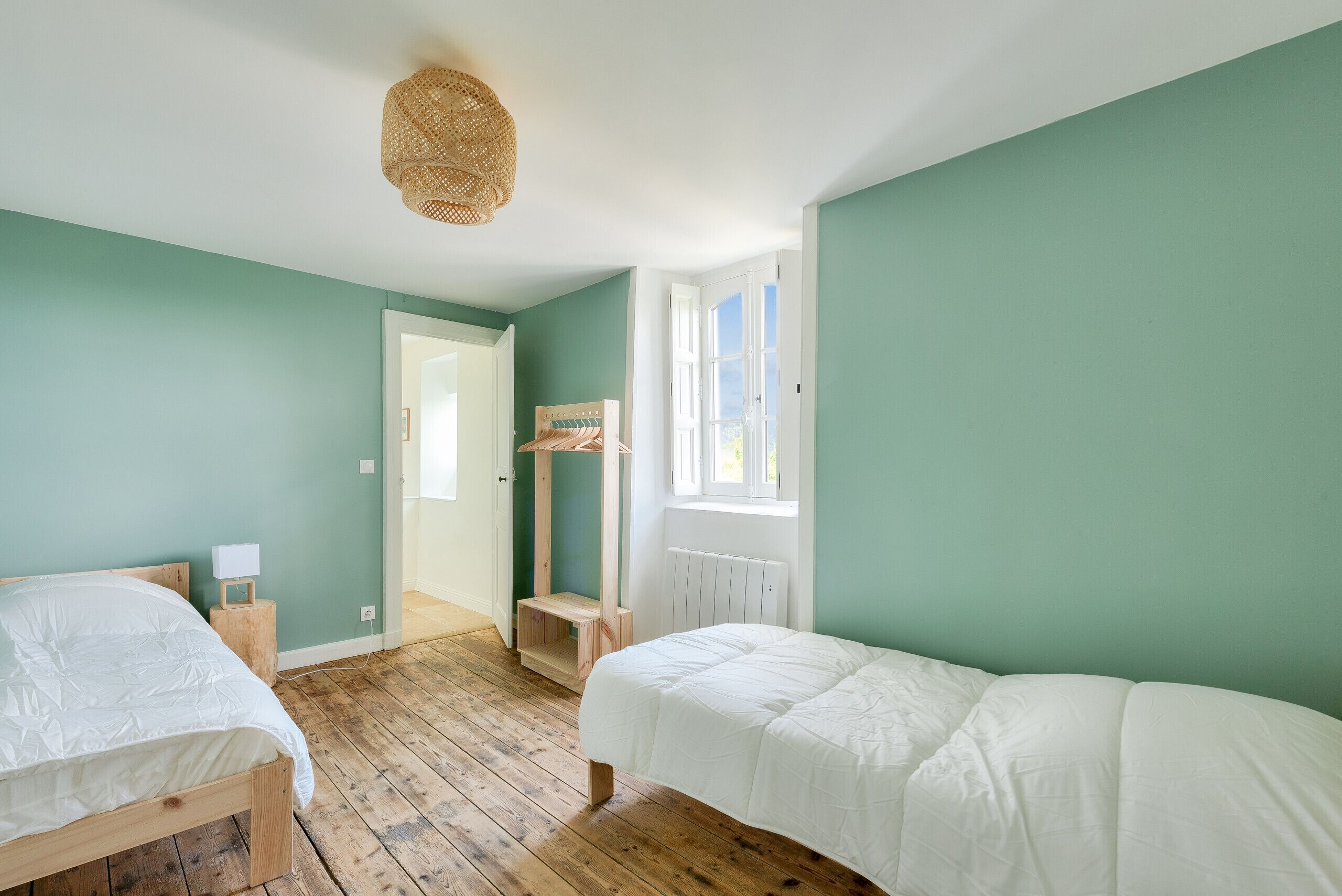 Een kamer met twee bedden, een houten vloer, een raam en een deur.