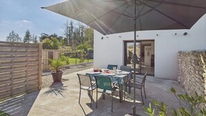 En udendørs terrasse med et bord og stole under en stor parasol, omgivet af et træhegn og en stenvæg.