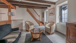En stue med sofa, to lænestole, et glasbord, en lampe, en trappe og et vindue med udsigt.