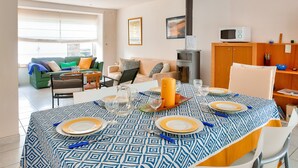 Un comedor con una mesa dispuesta para cuatro personas, una estufa de leña y un sofá verde al fondo.