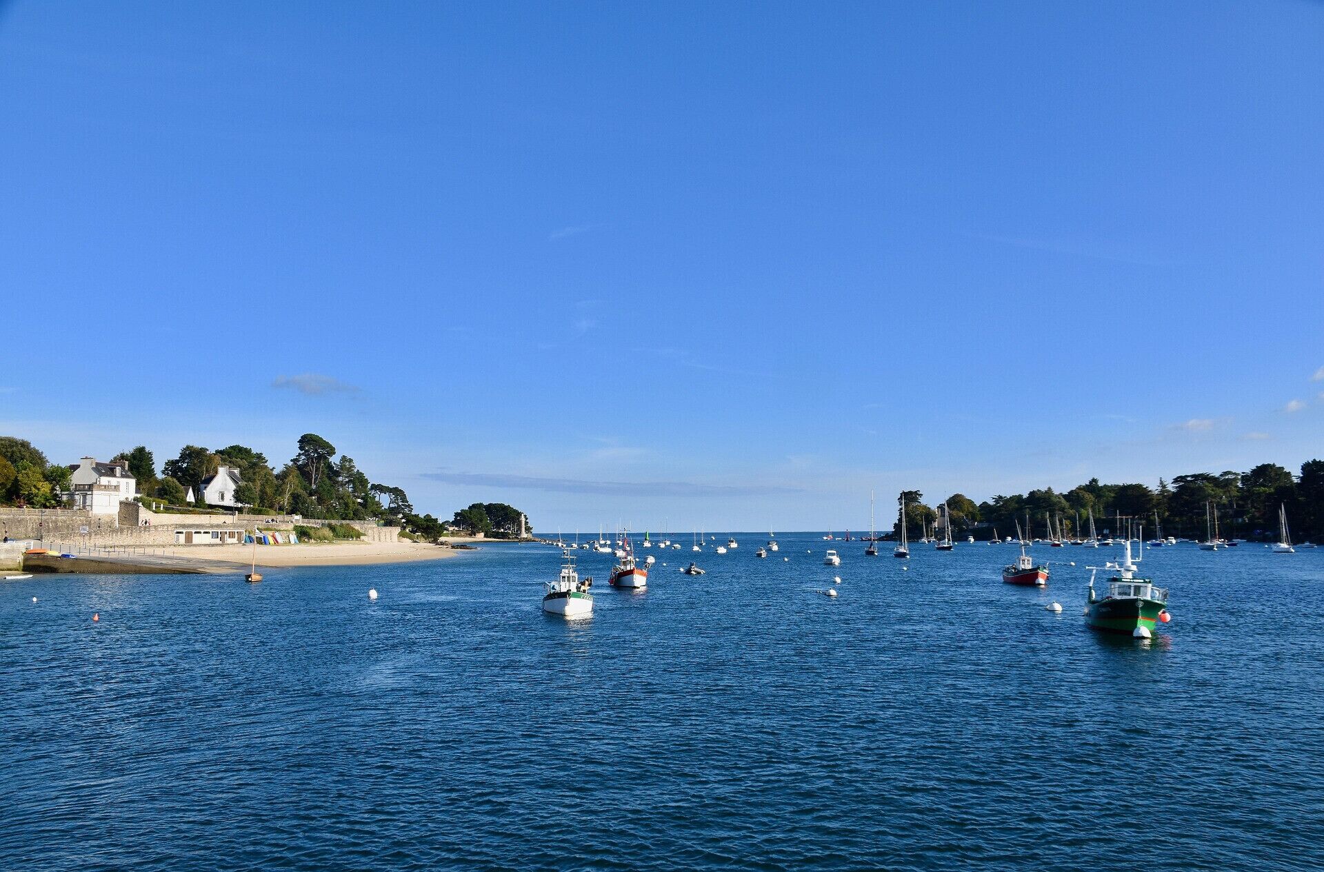 A coastal marina with boats docked and a sandy beach in the background.