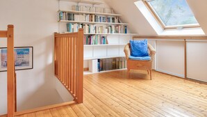 Una habitación con suelo de madera, una estantería, una silla y un tragaluz.