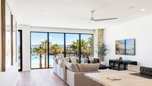 A spacious living area with a large window overlooking a pool and palm trees, a modern sofa, and a dining table.