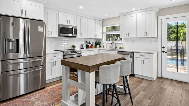 A modern kitchen with white cabinetry, stainless steel appliances, and a central island with bar stools. - Seminole Shores Haven - Heated Pool & Hot Tub (Seminole)