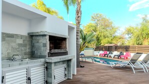 Ein Außenbereich mit Küche, einer Stein-Spritzschutzleiste, einem eingebauten Grill und einer Holzterrasse.