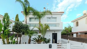 Ein modernes, zweistöckiges Haus mit weißer Fassade, einer schwarzen Tür und einem kleinen Balkon.