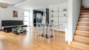 Ein modernes Wohnzimmer mit einem Glastisch, transparenten Stühlen, einem schwarzen Sofa und einer Treppe.