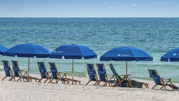 Een strand met rijen blauwe parasols en ligbedden.
