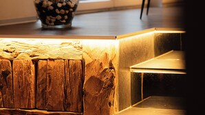 Een modern interieur met een houten bankje, een glazen vaas met gedroogde planten en een wanddecoratie met een geometrisch ontwerp.