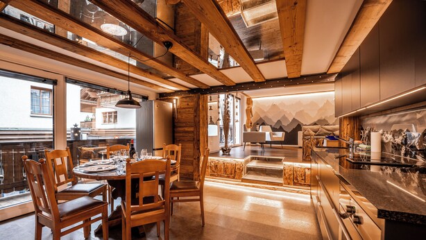Een moderne keuken met houten balken, een eethoek met houten stoelen en uitzicht op de bergen door de ramen.