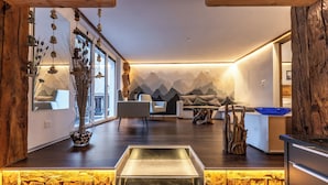 Een modern interieur met een houten accentmuur, een zithoek met een bank en stoelen, een keuken met een blauw aanrecht, en een decoratieve plantencompositie.