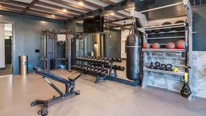 A gym with weightlifting equipment, a punching bag, and kettlebells. - Comfortable 1BR Suite w Pool, Parking, Gym 08 (Dallas)