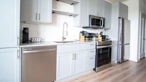 A modern kitchen with grey cabinets, stainless steel appliances, and a wooden floor. - Comfortable 1BR Suite w Pool, Parking, Gym 08 (Dallas)