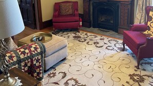 A living room with a fireplace, a red armchair, a sofa, a lamp, and a patterned rug. - Beautiful King Size Bed, private bath and breakfast included (Canandaigua)