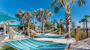A hammock area with striped fabric, surrounded by palm trees and a sandy beach.