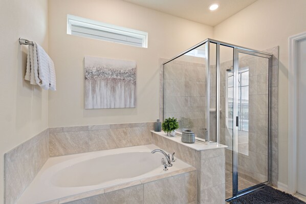 A modern bathroom with a freestanding bathtub, a glass-enclosed shower, and a marble-tiled wall.