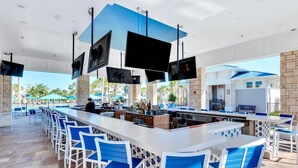 A bar area with multiple seating options, a counter with a bartender, and a poolside view.